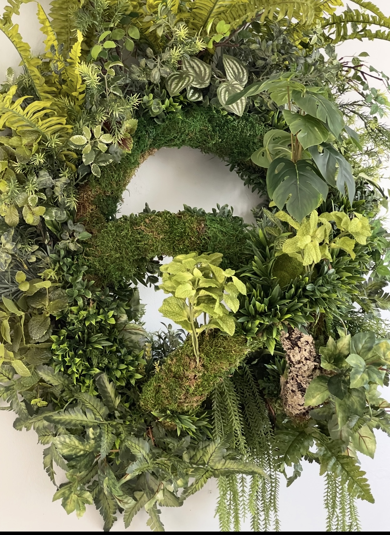 Biophilic Design — full green wreath with moss and monstera on a white wall.